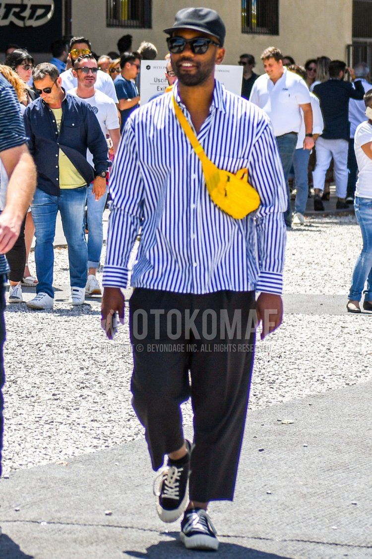 Men's spring/summer coordinate and outfit with plain black baseball cap, plain black sunglasses, blue striped shirt, dark gray plain wide pants, black low-cut sneakers, and plain yellow body bag.