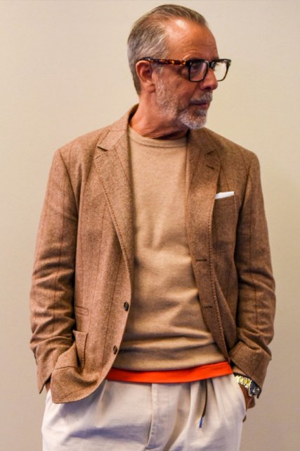 Men's spring and fall coordinate and outfit with brown tortoiseshell glasses, beige striped tailored jacket, solid beige sweater, solid orange t-shirt, solid white cotton pants, solid orange socks, and suede beige plain toe leather shoes.