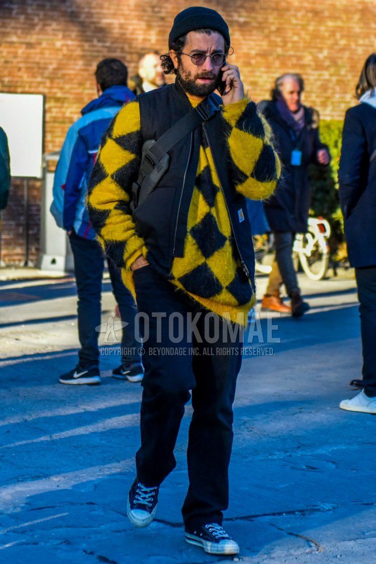 Men's winter coordinate and outfit with plain black knit cap, plain sunglasses, yellow top/inner sweater, plain black casual vest, plain black cotton pants, and black low-cut Converse sneakers.