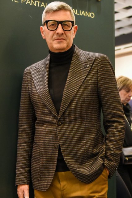 Men's spring and fall coordinate and outfit with plain black glasses, gray checked tailored jacket, plain black turtleneck knit, plain beige cargo pants, plain black socks, and brown wingtip leather shoes.