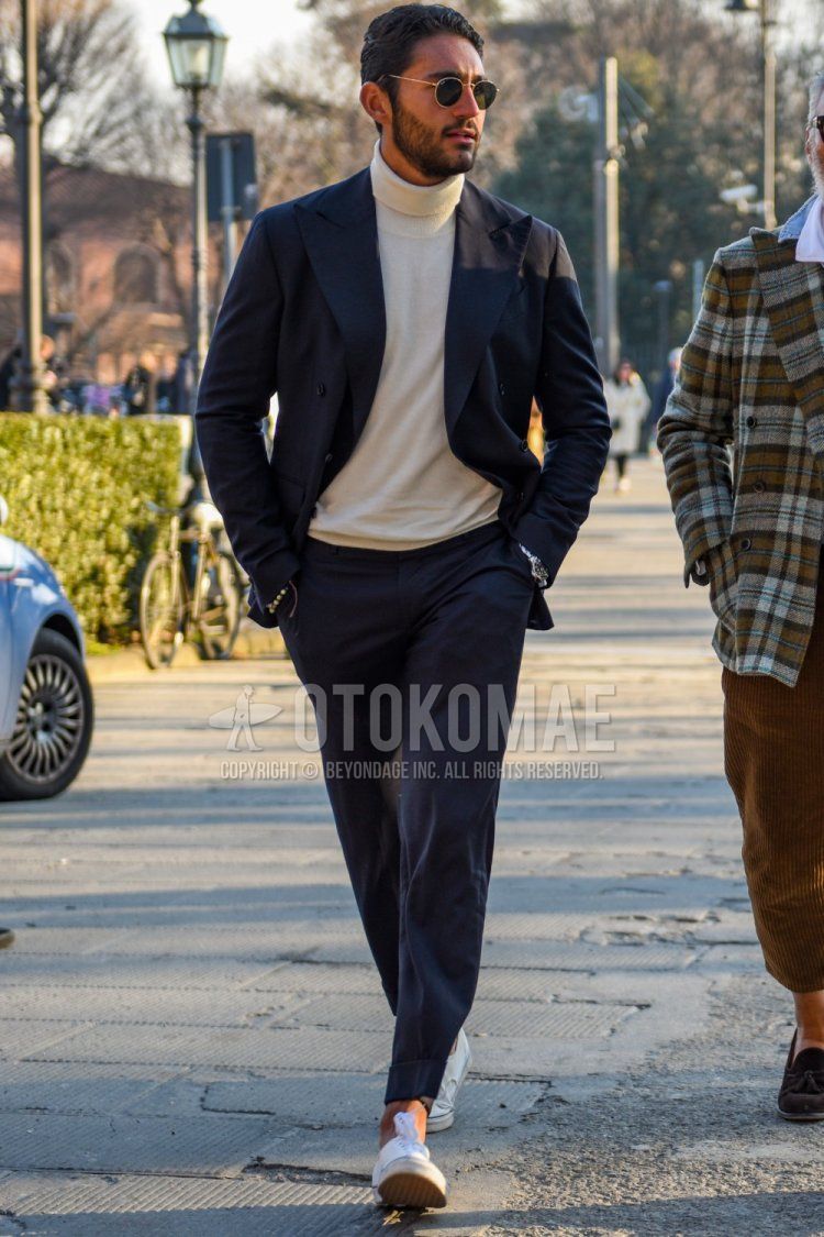 Men's spring and fall coordinate and outfit with round solid gold sunglasses, solid white turtleneck knit, white low-cut sneakers, and solid navy suit.