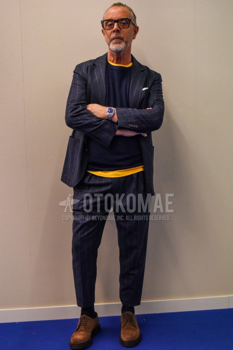 Men's spring and fall coordinate and outfit with brown tortoiseshell glasses, plain navy sweater, plain yellow t-shirt, plain black socks, suede brown plain toe leather shoes, and navy striped suit.