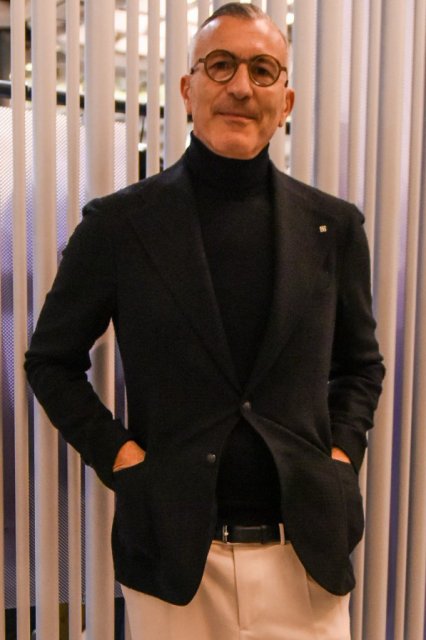 Men's spring and fall coordinate and outfit with brown tortoiseshell glasses, plain black tailored jacket, plain black turtleneck knit, plain black leather belt, plain white cotton pants, and black straight tip leather shoes.