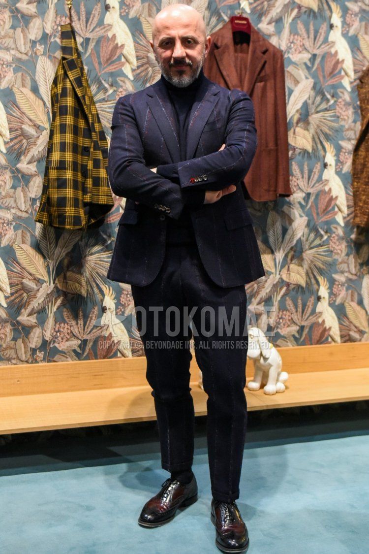 Men's spring and fall coordinate and outfit with plain black turtleneck knit, plain black socks, brown wingtip leather shoes, and dark gray striped suit.