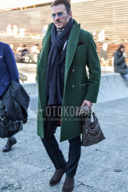 Men's fall/winter outfit with solid gold sunglasses, solid gray scarf/stall, solid green chester coat, suede brown hall-cut leather shoes, solid brown briefcase/handbag, and gray striped suit.
