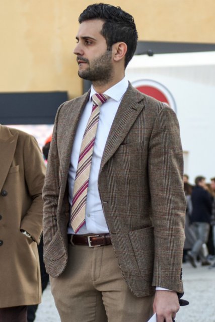 Men's spring and fall outfit with beige checked tailored jacket, plain white shirt, plain brown leather belt, plain beige slacks, brown boots, and beige regimental tie.