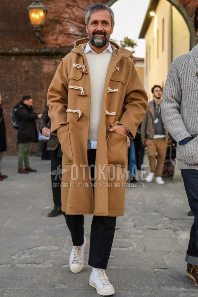 Undercover men's fall/winter outfit with solid beige duffle coat, solid white sweater, solid white shirt, dark gray solid slacks, dark gray solid cropped pants, and white high-cut sneakers.