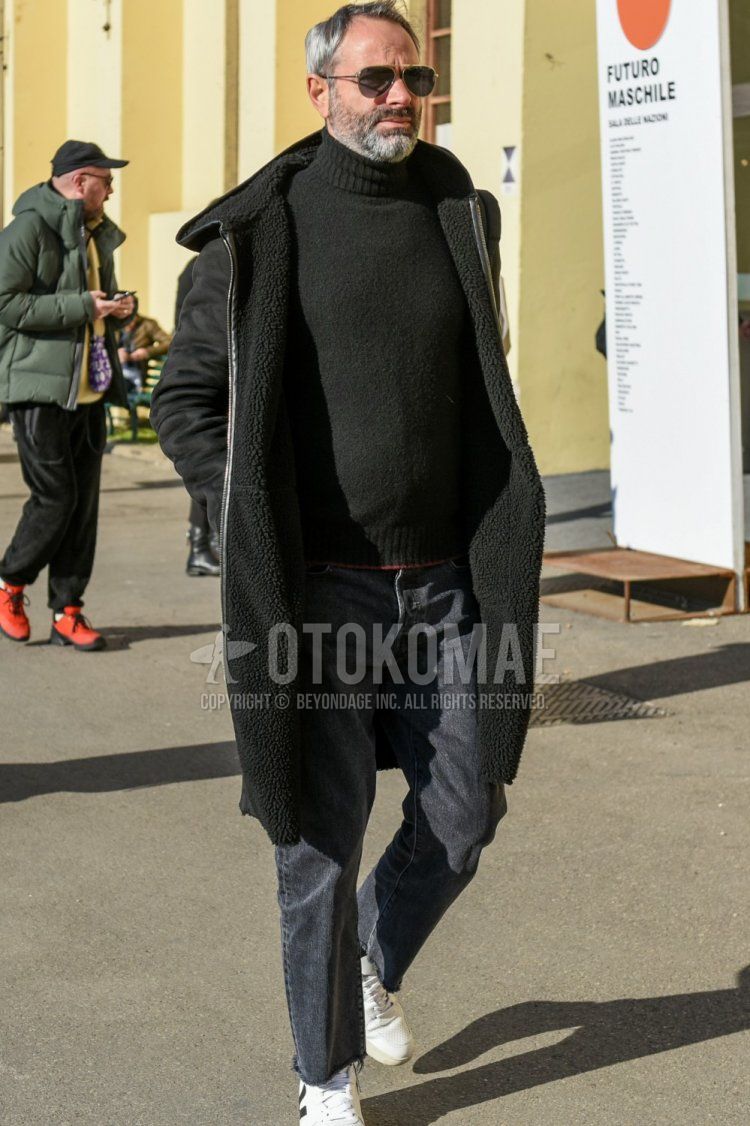 Men's fall/winter coordinate and outfit with teardrop gold solid sunglasses, solid black hooded coat, solid black turtleneck knit, solid gray denim/jeans, and white low-cut sneakers.