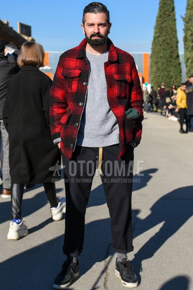 Men's fall/winter outfit/clothing with red/black checked shirt jacket, solid gray sweater, dark gray solid slacks, gray socks socks, and black low-cut sneakers.