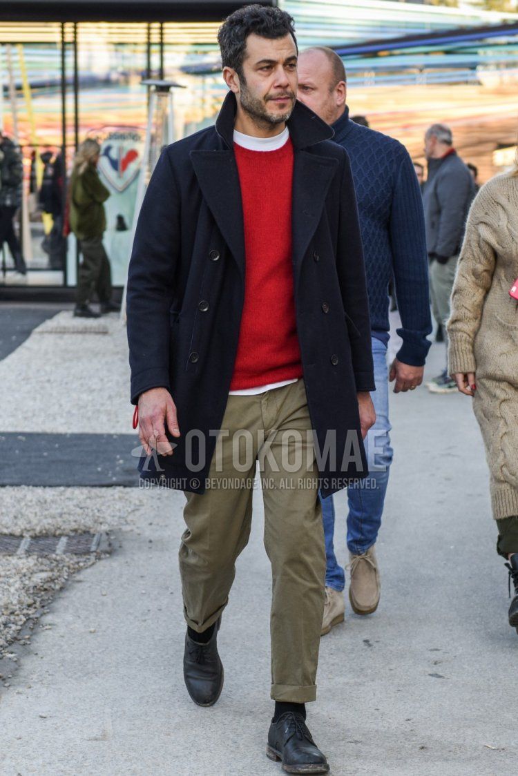 Men's fall/winter outfit with dark gray solid color chester coat, red solid color sweater, white solid color t-shirt, beige solid color chinos, black solid color socks, and black plain toe leather shoes.