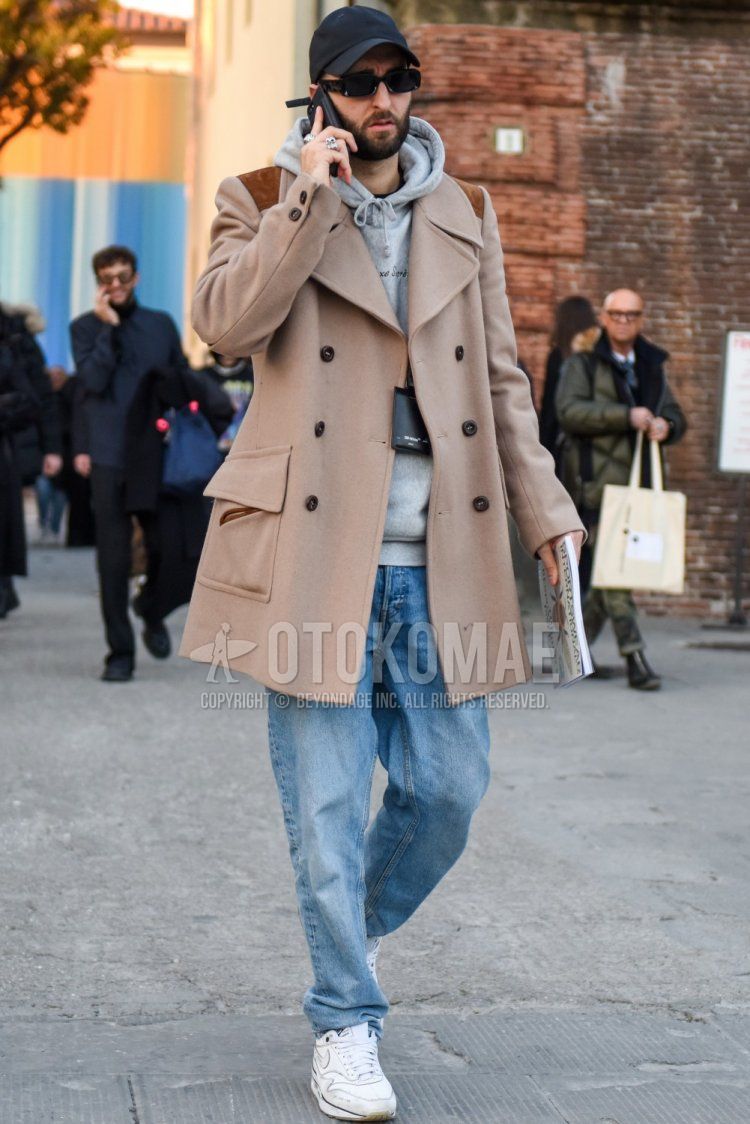 Men's fall/winter coordinate and outfit with dark gray solid color baseball cap, black solid color sunglasses, beige solid color P-coat, gray solid color hoodie, blue solid color denim/jeans, and white low-cut Nike sneakers.