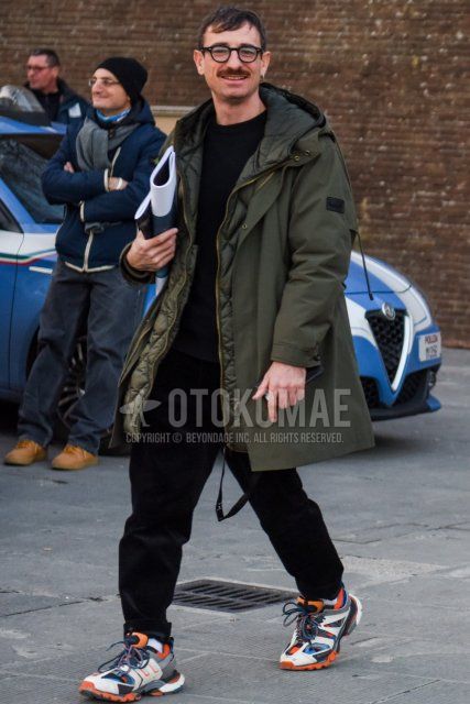 Men's fall/winter coordinate and outfit with plain black glasses, plain olive green hooded coat, plain black sweater, plain black cotton pants, plain white socks, and Balenciaga track trainers with multi-colored low-cut sneakers.