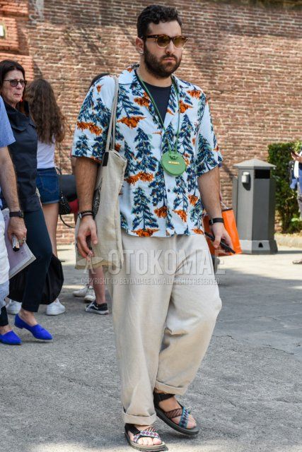 Men's summer coordinate and outfit with brown tortoiseshell sunglasses, Acne Studios multi-colored botanical shirt, plain navy t-shirt, plain beige wide-leg pants, and multi-colored sport sandals.