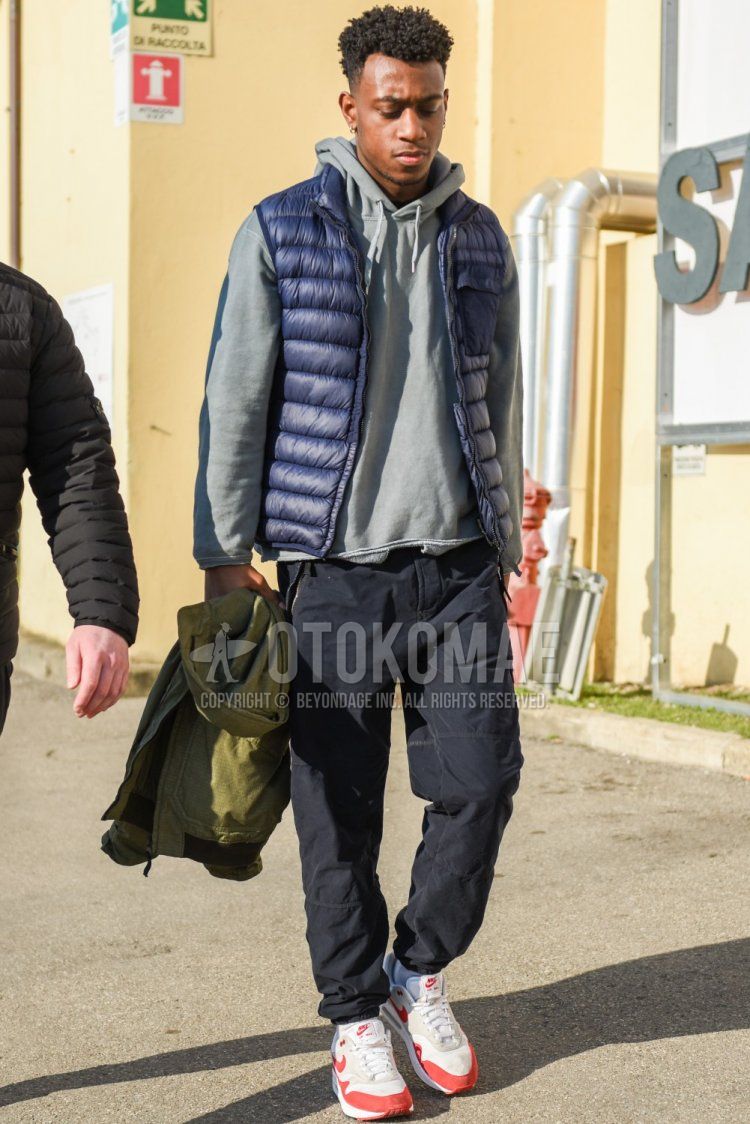 Men's fall/winter outfit with plain navy down jacket, plain navy casual vest, plain gray hoodie, plain navy chinos, plain white socks, and Nike Air Max 1 gray/red low-cut sneakers.