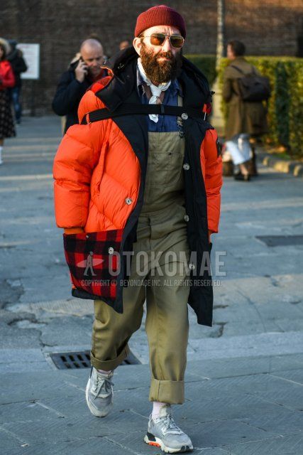 Red solid knit cap, gold solid sunglasses, white solid bandana/neckerchief, orange solid hooded coat, orange solid down jacket, overalls beige solid jumpsuit, gray solid shirt, beige solid sweater, white solid socks, Gray low-cut sneakers with a winter men's outfit/coat.