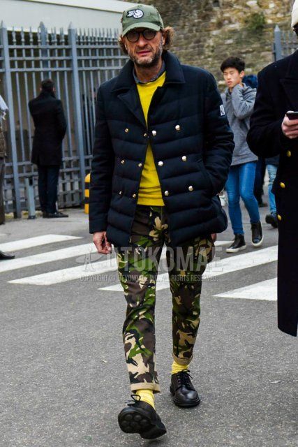 Winter men's coordinate and outfit with olive green one-pointed baseball cap, solid navy down jacket, solid yellow sweater, multi-colored camouflage cargo pants, solid yellow socks, and black plain toe leather shoes.