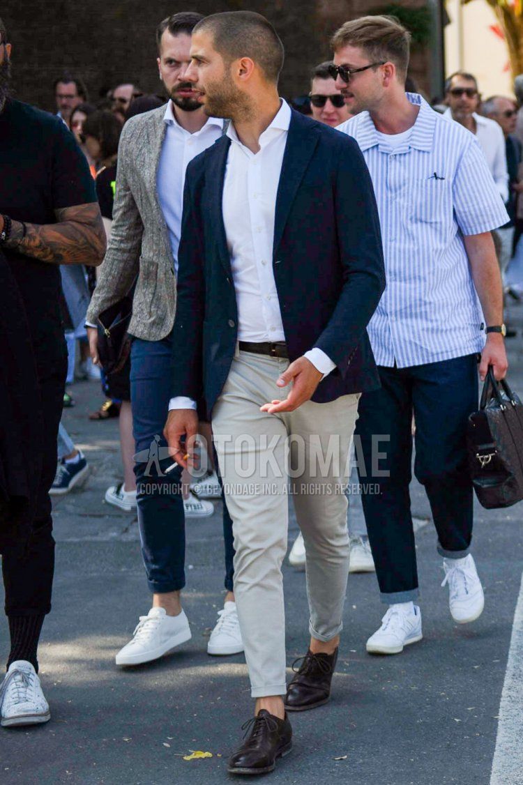 Men's spring, summer, and fall outfit with plain navy tailored jacket, plain white shirt, plain brown leather belt, plain beige cotton pants, and brown plain toe leather shoes.