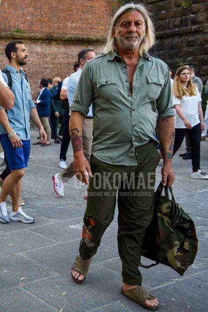 Summer men's coordinate and outfit with plain green shirt, plain olive green easy pants, plain chinos, beige leather sandals, and olive green camouflage briefcase/handbag.