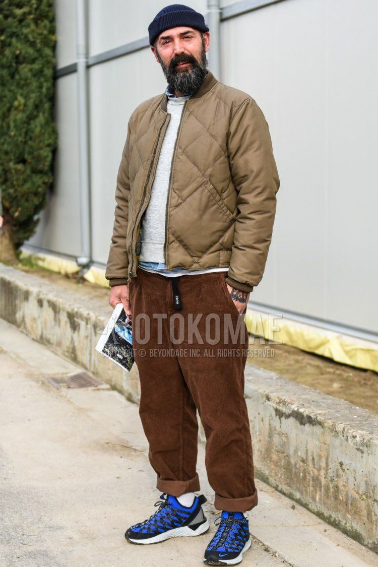 Men's fall/winter coordinate and outfit with solid black knit cap, solid beige down jacket, solid gray sweatshirt, solid light blue denim/chambray shirt, solid brown winter pants (corduroy, velour), solid white socks, Nike blue low cut sneakers.