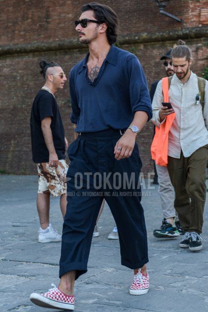 Summer men's coordinate and outfit with plain black sunglasses, plain navy polo shirt, plain navy beltless pants, plain cropped pants, and Vans red and white low-cut sneakers.