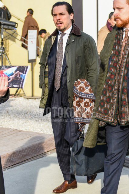 Autumn/winter men's coordinate and outfit with a plain olive green olive green field jacket/hunting jacket from Babur, plain white shirt, plain navy socks, brown coin loafer leather shoes, gray striped suit, and a multi-colored tie.