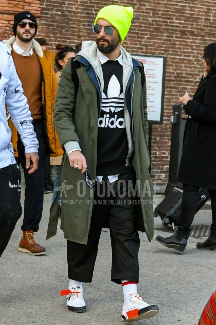 Fall/Winter with solid yellow knit cap, solid gold sunglasses, solid olive green stainless coat, solid gray hoodie, Adidas black decal logo sweatshirt, solid white shirt, solid black chinos, solid white socks, off white white low-cut sneakers Men's coordination and dressing for fall/winter.