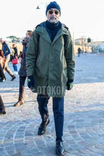 Men's fall/winter coordinate and outfit with solid navy knit cap, solid beige sunglasses, solid olive green hooded coat, solid gray turtleneck knit, gray striped slacks, solid black socks, and black wingtip leather shoes.
