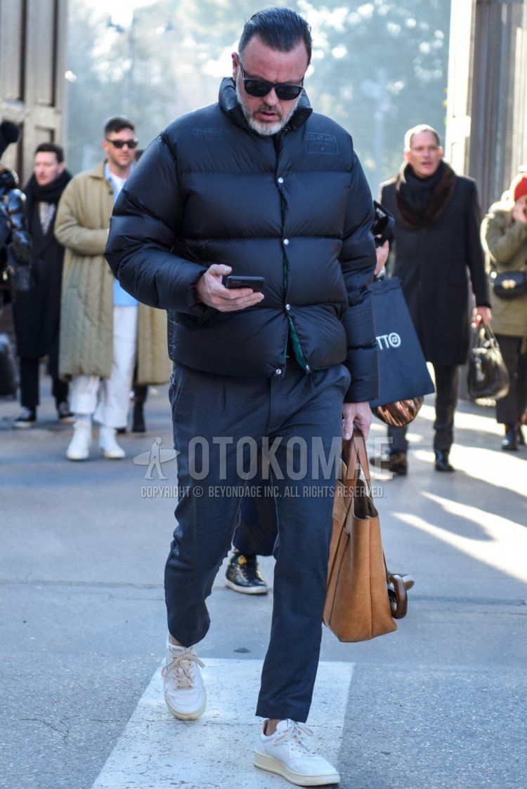 Winter men's outfit/clothing with solid black sunglasses, solid black down jacket, solid gray ankle pants, solid gray pleated pants, solid gray slacks, white low-cut sneakers, and solid beige briefcase/handbag.
