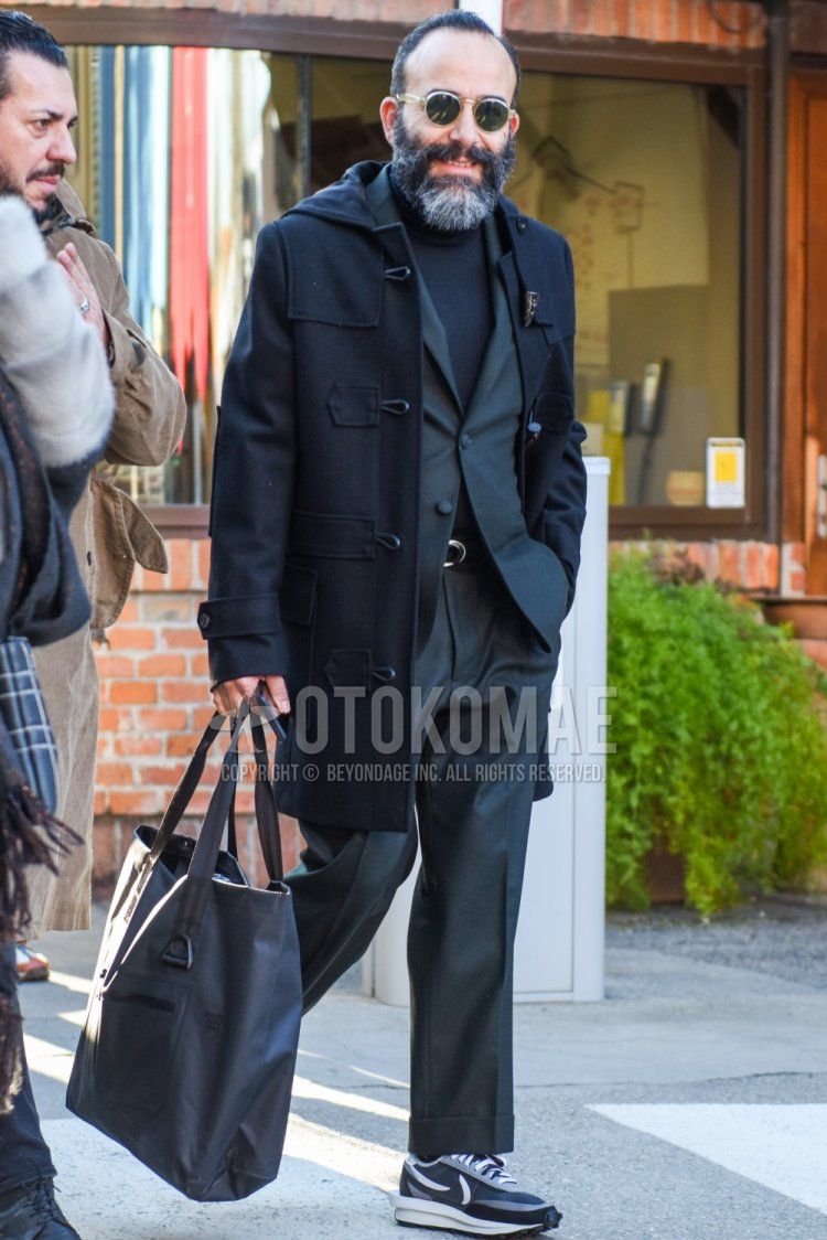 Men's fall/winter outfit/clothing with clear solid sunglasses, solid black duffle coat, dark gray solid turtleneck knit, Nike Sakai waffle gray low-cut sneakers, solid gray briefcase/handbag, and solid gray suit.
