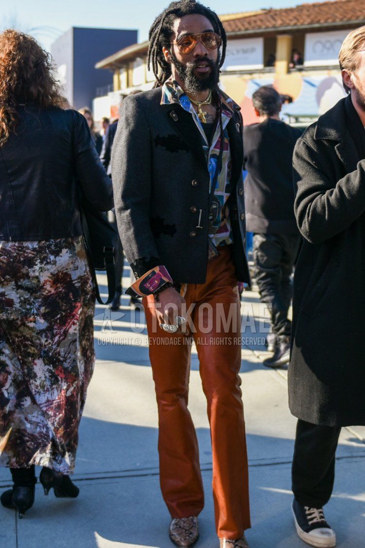 Men's spring, summer, and fall coordinate and outfit with teardrop gold solid sunglasses, solid gray tailored jacket, multi-colored top/inner shirt, solid orange bottoms, and brown boots.