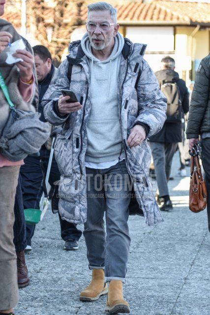 Winter men's coordinate and outfit with clear plain glasses, gray outer down jacket, gray one-pointed hoodie, gray plain denim/jeans, and suede beige side gore boots.