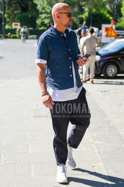 Summer men's coordinate and outfit with plain black sunglasses, navy striped shirt, plain white t-shirt, dark gray plain slacks, and white high-cut Converse All Star sneakers.