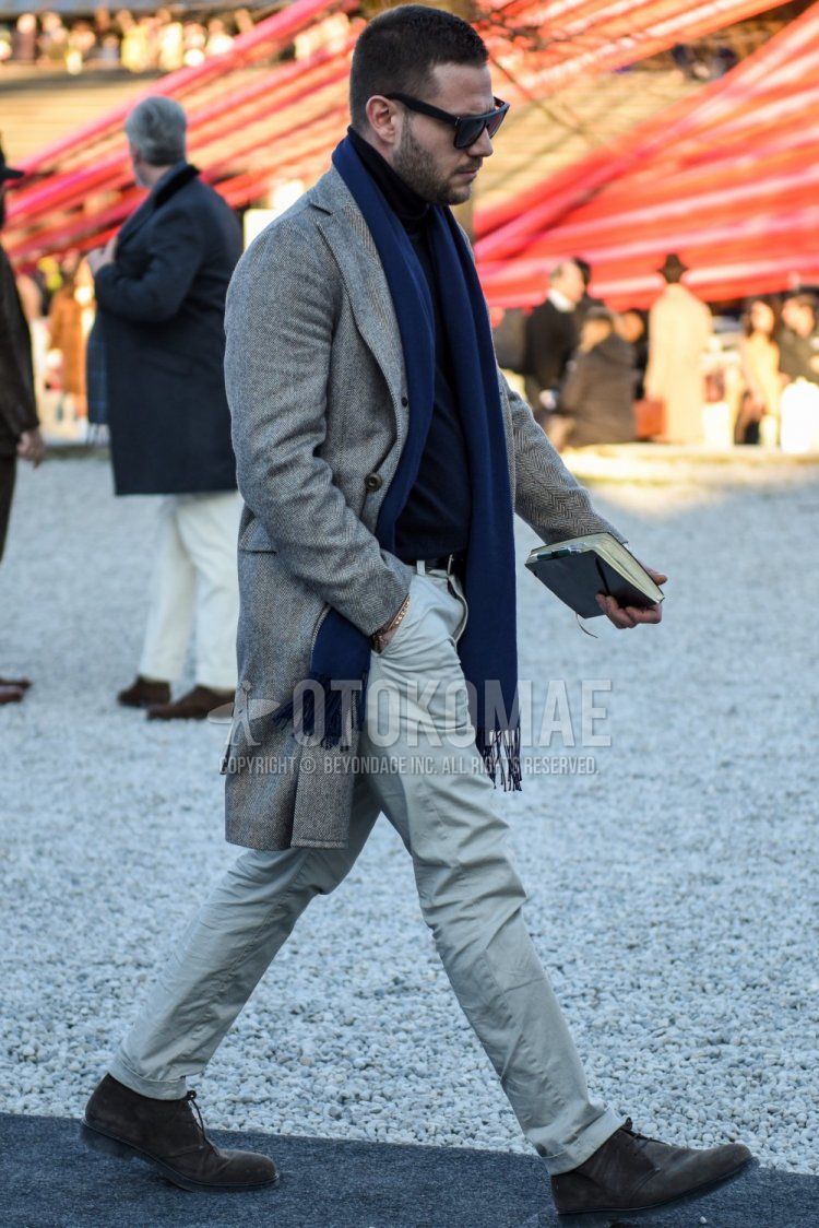 Men's fall/winter outfit with solid black sunglasses, solid navy scarf/stall, gray herringbone chester coat, solid black turtleneck knit, solid black leather belt, solid beige chinos and suede brown boots.