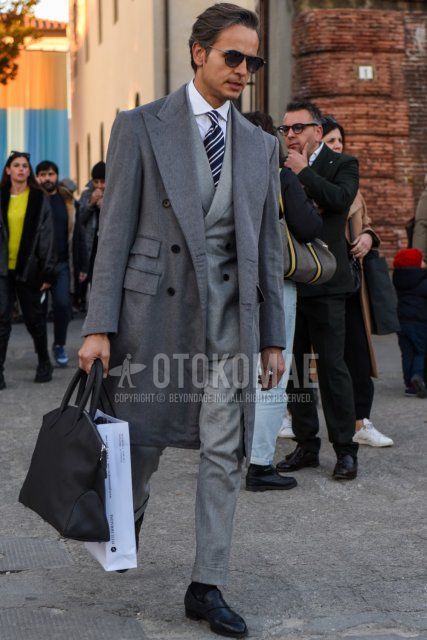 Winter/fall men's coordinate/outfit with teardrop solid black sunglasses, solid gray chester coat, solid white shirt, solid black socks, black leather shoes, solid black briefcase/handbag, solid gray suit, and navy regimental tie.