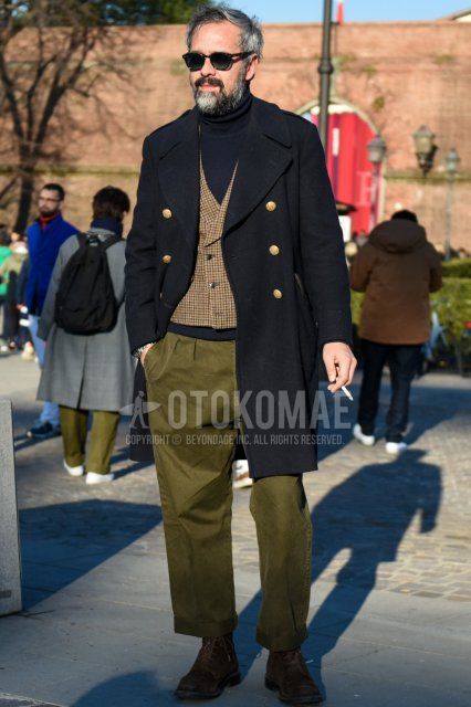 Men's fall/winter outfit and outfit in Boston with plain black sunglasses, plain black Ulster coat, brown checked gilet, plain navy turtleneck knit, plain olive green chinos, plain olive green pleated pants, and brown boots.