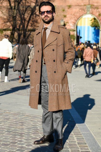 Men's fall/winter outfit with brown tortoiseshell sunglasses, brown checked trench coat, solid beige shirt, solid brown leather belt, solid gray slacks, solid gray ankle pants, brown boots, and solid brown tie.