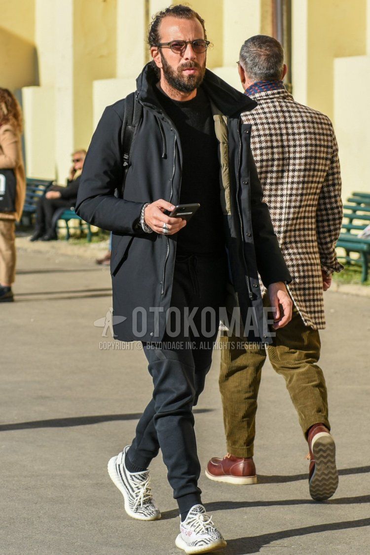 Men's fall/winter coordinate and outfit with clear solid glasses, solid black outerwear, solid black down jacket, solid black sweatshirt, solid black jogger pants/ribbed pants, solid black socks, and Adidas Easy Boost white low-cut sneakers.
