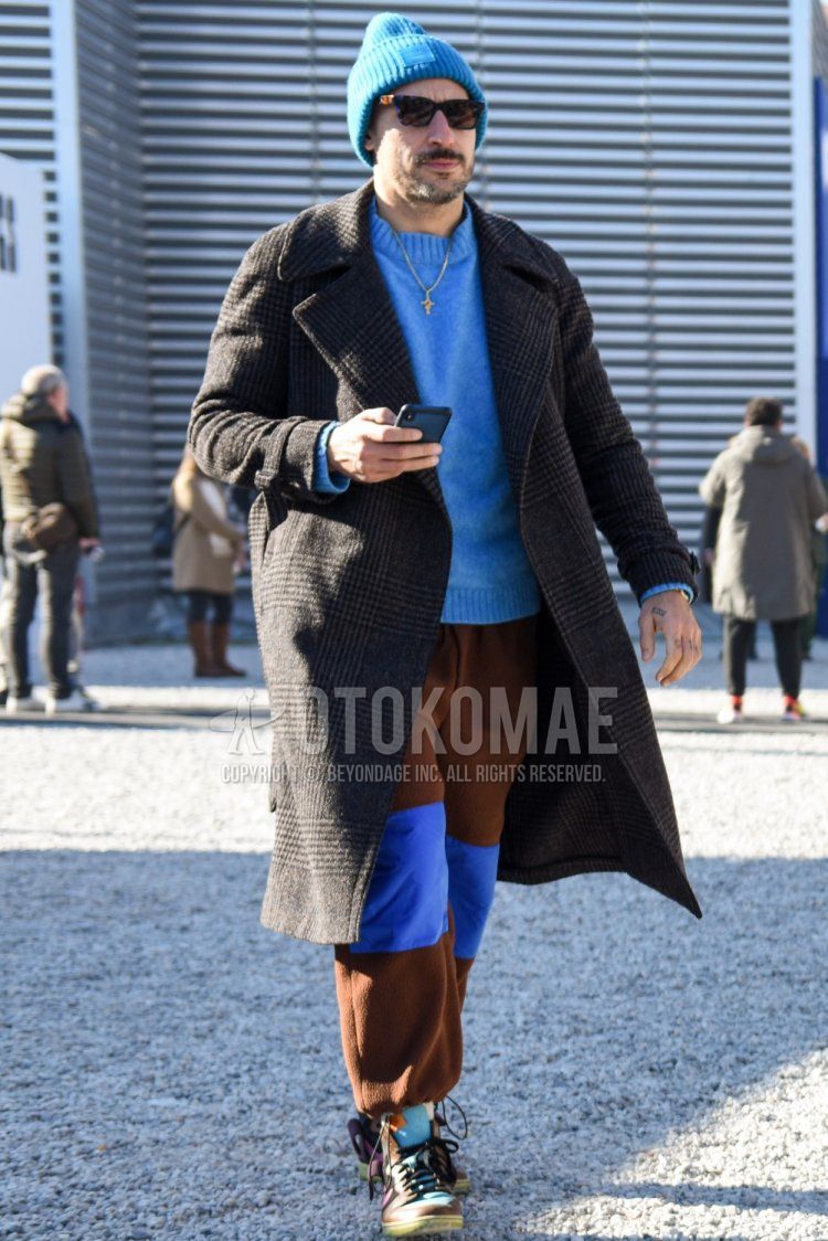 Men's fall/winter coordinate and outfit with plain blue hat, blue tortoiseshell sunglasses, gray checked trench coat, plain blue sweater, plain brown sweatpants, and multi-colored high-cut sneakers.