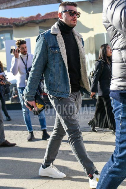 Men's fall/winter outfit with solid black sunglasses, solid blue denim jacket, solid black turtleneck knit, solid gray cotton pants, solid navy socks, white low-cut sneakers, Fendi black bag clutch/second bag/drawstring.