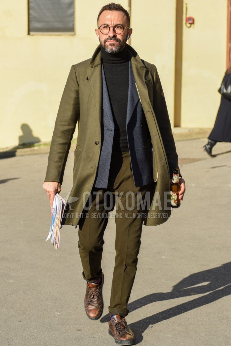 Men's fall/winter coordinate and outfit with plain black glasses, plain olive green chester coat, gray checked tailored jacket, plain black turtleneck knit, plain olive green slacks, multi-colored socks, brown low-cut sneakers.
