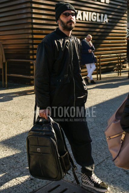 Men's fall/winter outfit and outfit with black one-pointed knit cap, solid black sunglasses, solid black MA-1, solid black slacks, Vans Skehai white and black high-cut sneakers, and solid black backpack.