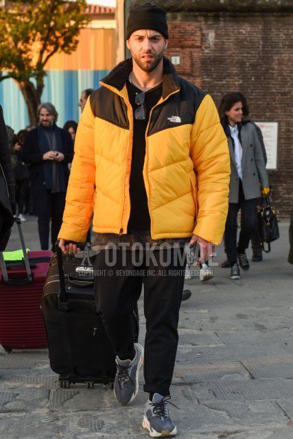 Men's fall coordinate and outfit with plain black knit cap, plain yellow/black down jacket, plain black sweater, plain black cotton pants, plain black socks, and gray low-cut sneakers.