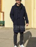 Men's fall/winter outfit with beige tortoiseshell sunglasses, solid navy duffle coat, solid black polo shirt, dark gray solid chinos, solid black socks, and white low-cut Adidas sneakers.