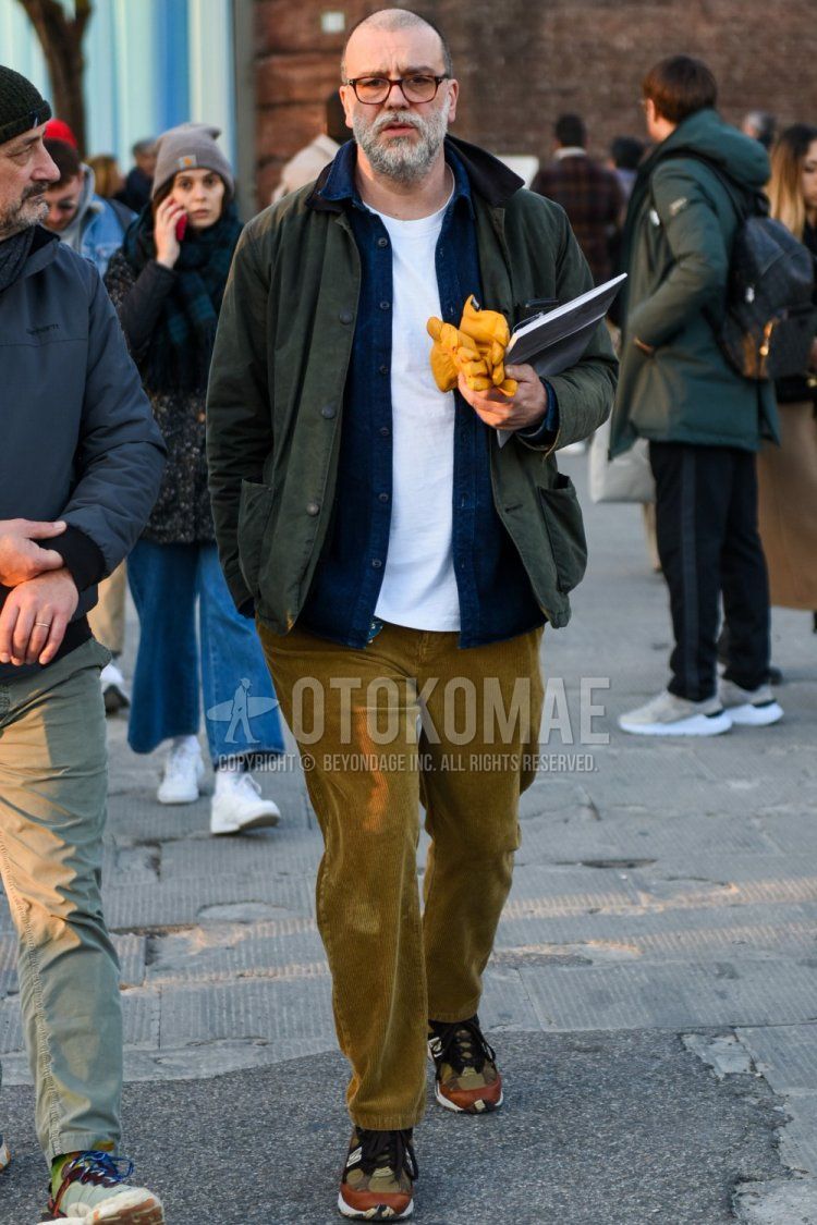Men's fall/winter coordinate with brown tortoiseshell glasses, olive green solid coveralls, solid navy shirt, solid white t-shirt, solid beige winter pants (corduroy, velour), solid beige ankle pants, brown low-cut sneakers by New Balance 991 How to wear.