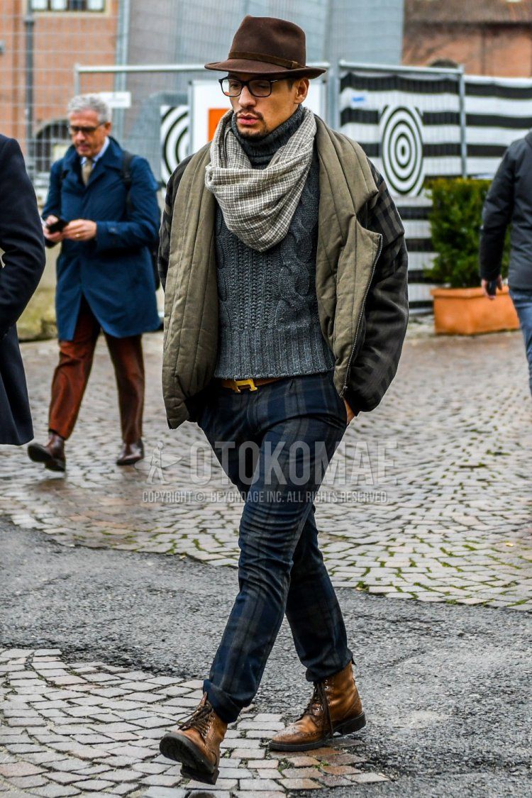Men's winter outfit and outfit with plain brown hat, plain black glasses, grey checked snood, plain olive green outerwear, plain grey turtleneck knit, plain brown leather belt from Hermes, navy/grey checked slacks and brown boots.