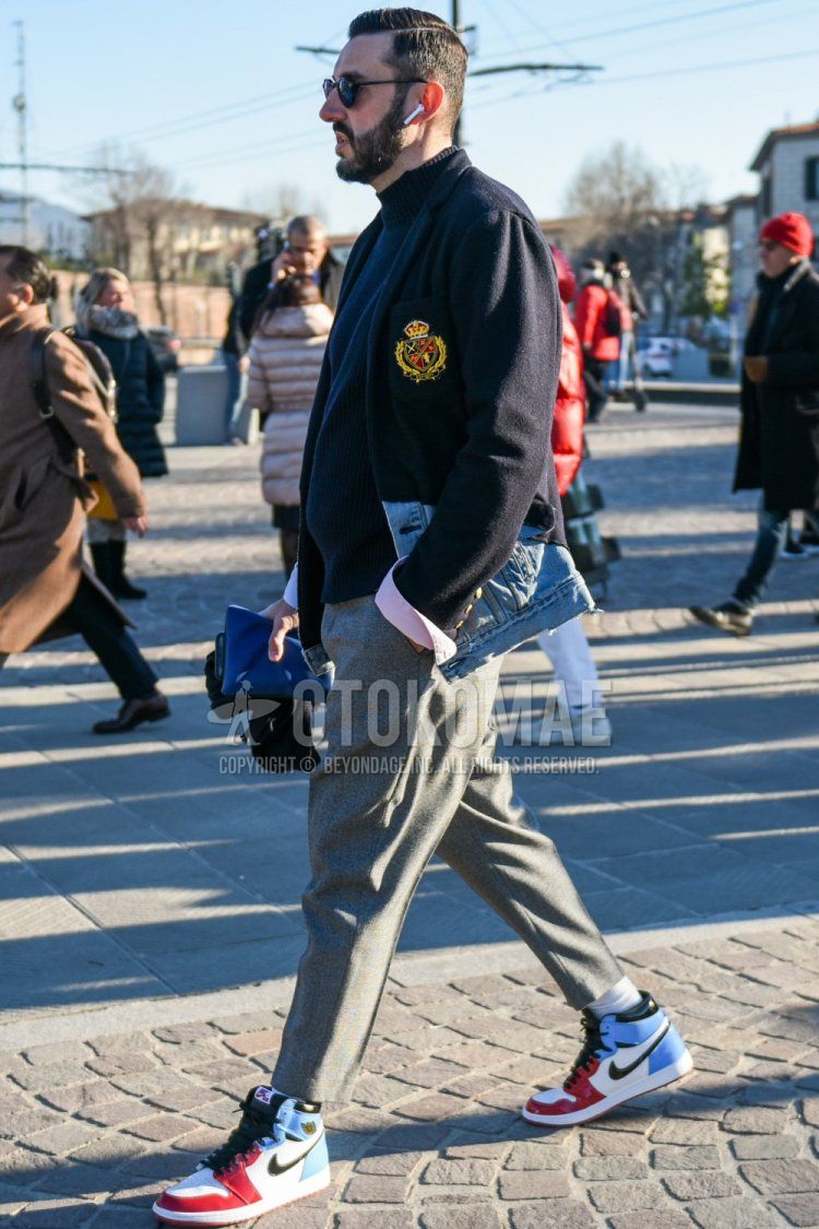 Men's spring and fall outfit with plain black sunglasses, plain navy tailored jacket, plain black turtleneck knit, plain gray slacks, plain gray cropped pants, and Nike Air Jordan 1 red and light blue high-cut sneakers.