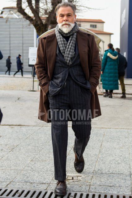 Men's fall/winter outfit with gray checked scarf/stall, plain brown trench coat, brown boots, and gray striped suit.