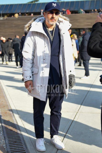 Winter men's coordinate and outfit with navy baseball cap, plain silver sunglasses, multi-colored scarf/stall, plain white down jacket, white low-cut sneakers, and navy striped suit.