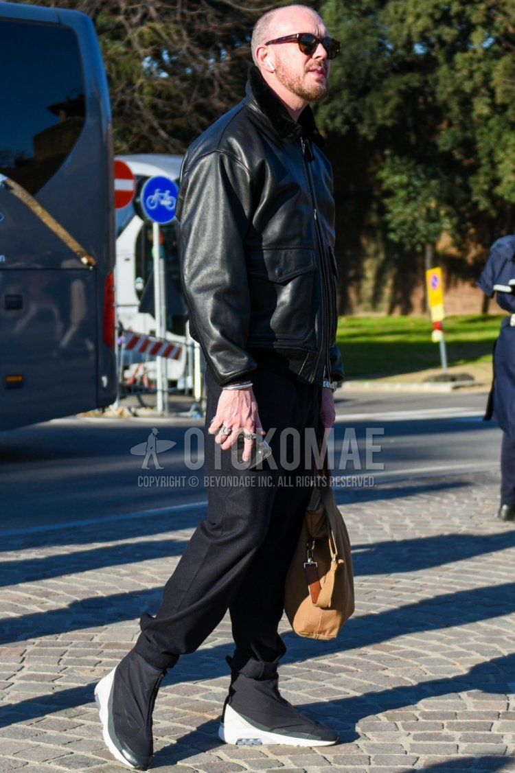 Men's fall/winter outfit with brown tortoiseshell sunglasses, plain black leather jacket (not rider), dark gray plain slacks, Nike Ambush Air Max 180 black high cut sneakers, beige plain briefcase/handbag.