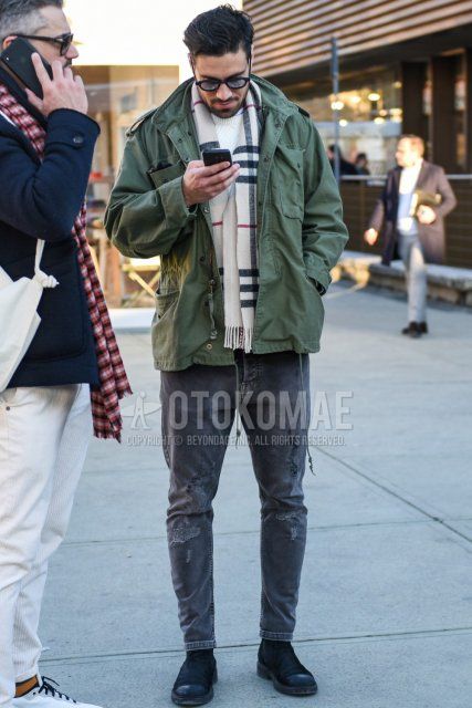 Men's fall/winter outfit/coordination with plain black sunglasses, white checked scarf/stall, plain olive green M-65, plain white sweater, plain gray denim/jeans, plain gray cropped pants, and suede black side gore boots.